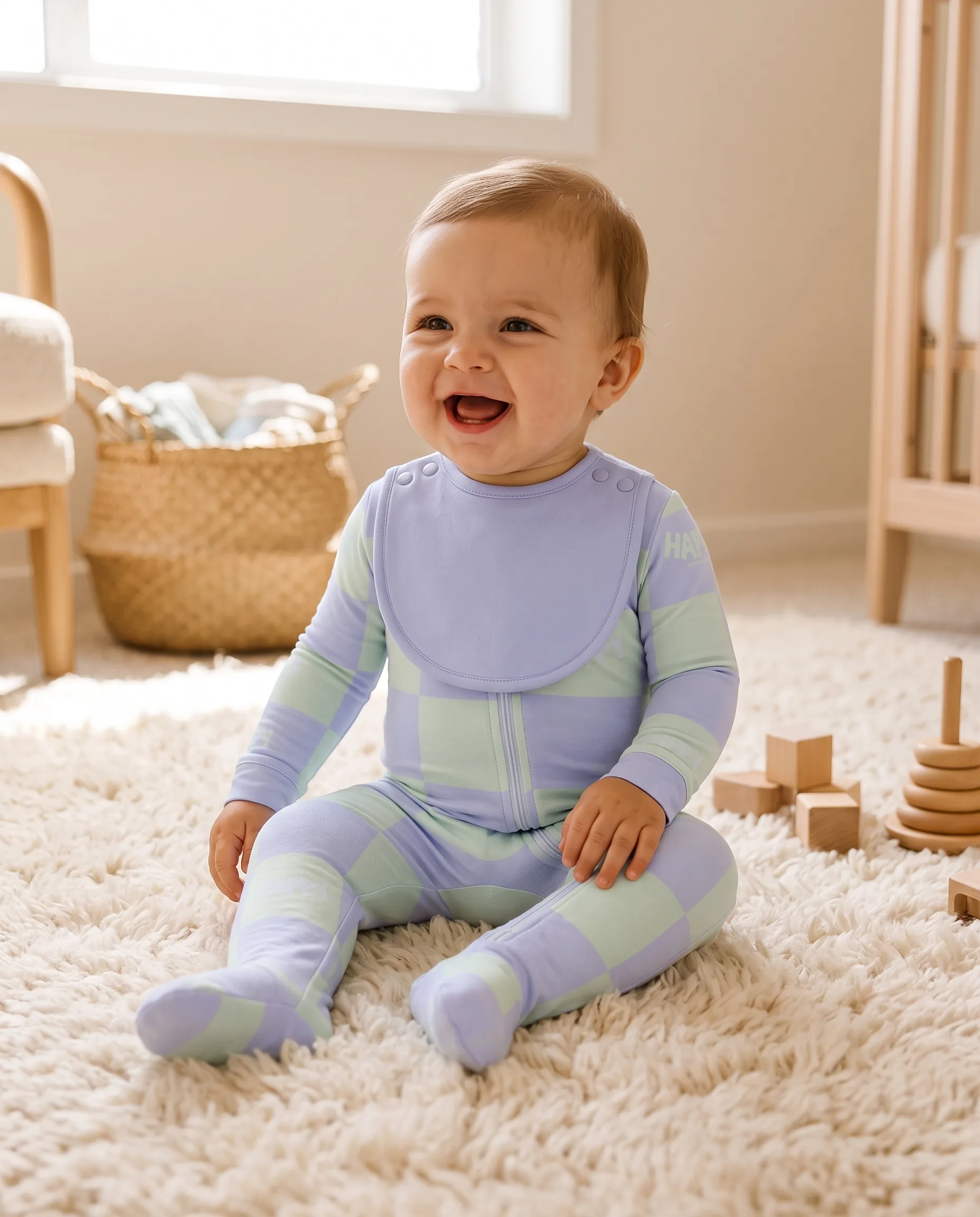 A laughing baby sitting on a cream rug in the Dream Garden Everything Zippy with the matching bib