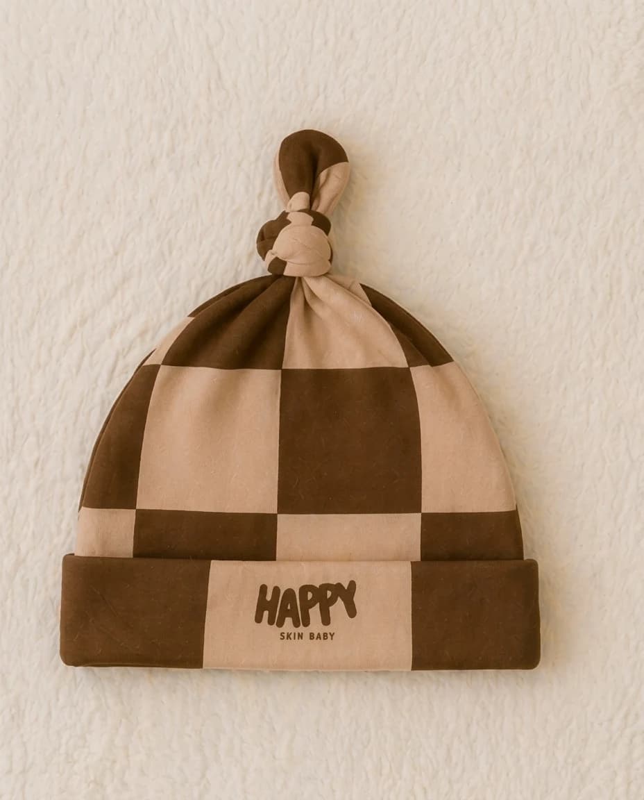 Cocoa Cozy checker knot hat with a HAPPY cuff on a cream blanket